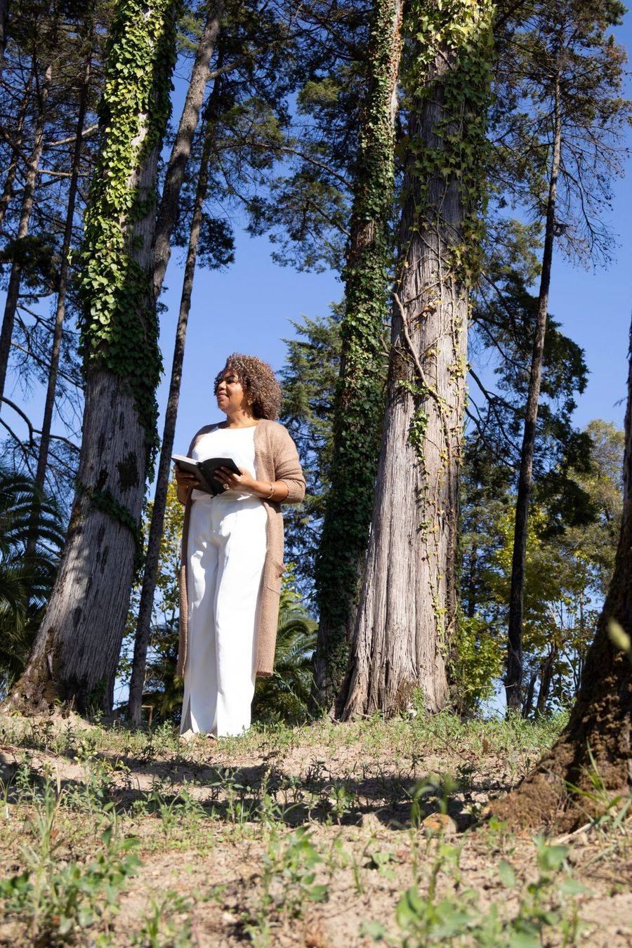 Valéria Araújo com um livro aberto em meio a árvores altas